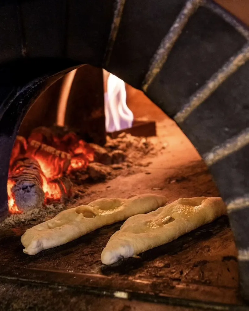 Pão a cozer dentro do forno a lenha, com a chama ao lado
